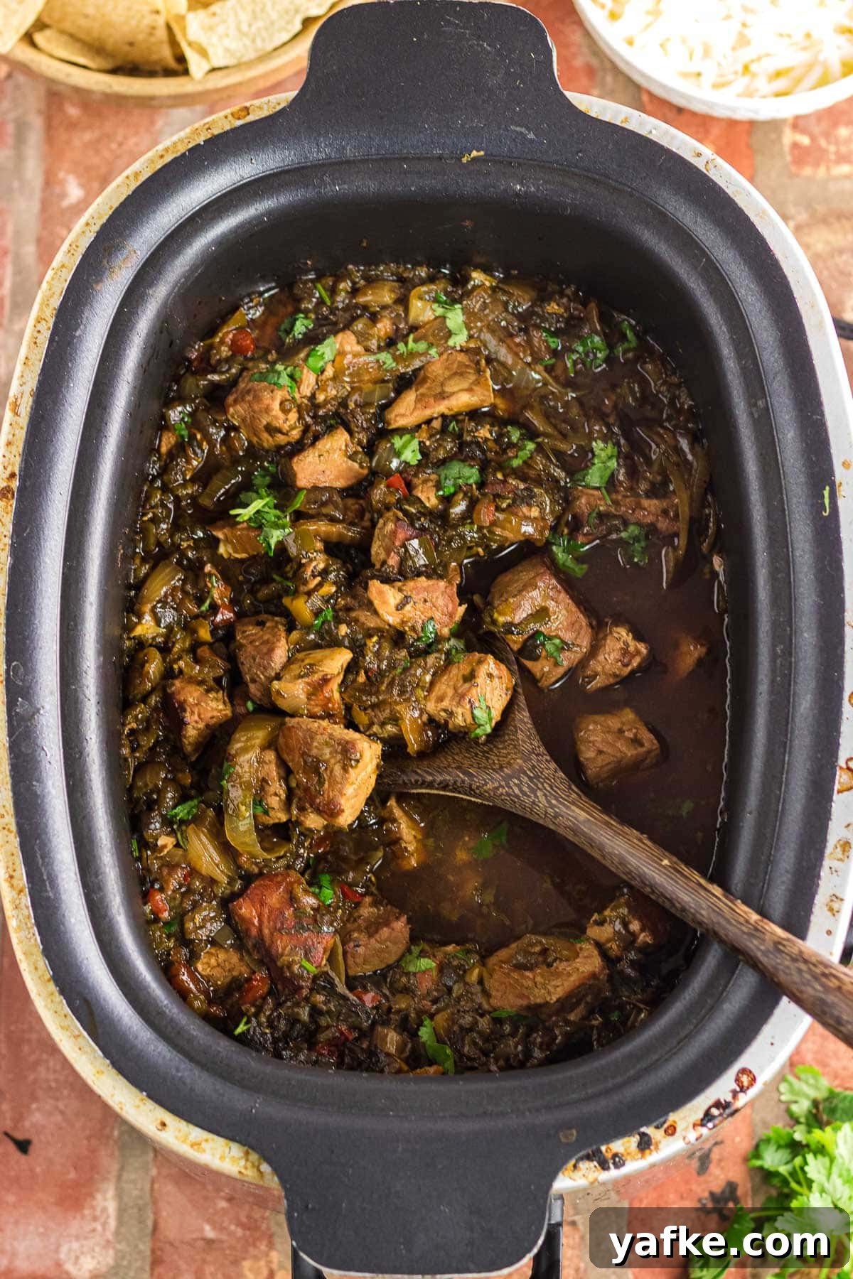 Slow Cooker Pork Chile Verde: Tender Pork in Tomatillo Sauce 2 Overhead view of pork chile verde in the slow cooker with a wooden serving spoon.
