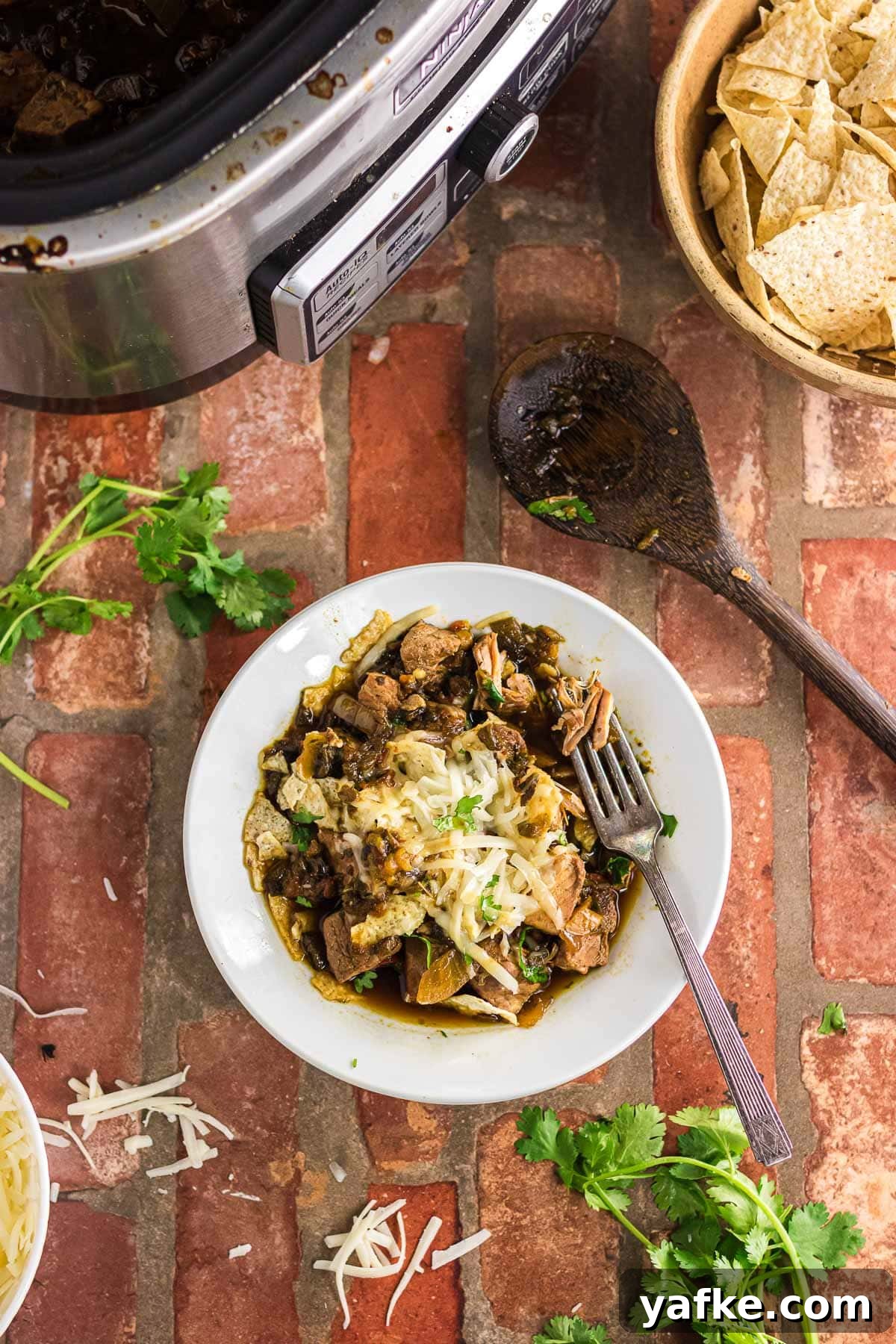 Slow Cooker Pork Chile Verde: Tender Pork in Tomatillo Sauce 8 A dinner bowl with pork chile verde topped with cheese and more cilantro.