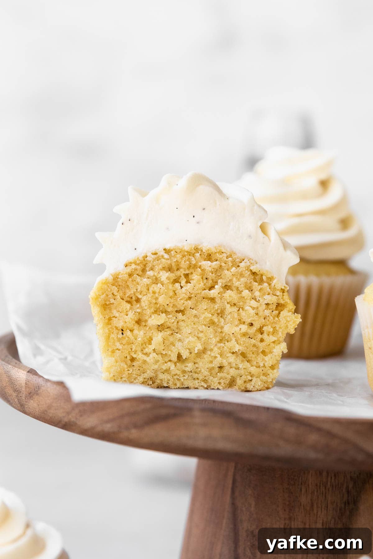How to Make Dairy-Free Cupcakes 11 A dairy free vanilla cupcake topped with dairy free vanilla buttercream on a wooden stand, sliced in half to show the fluffy and tender crumb.