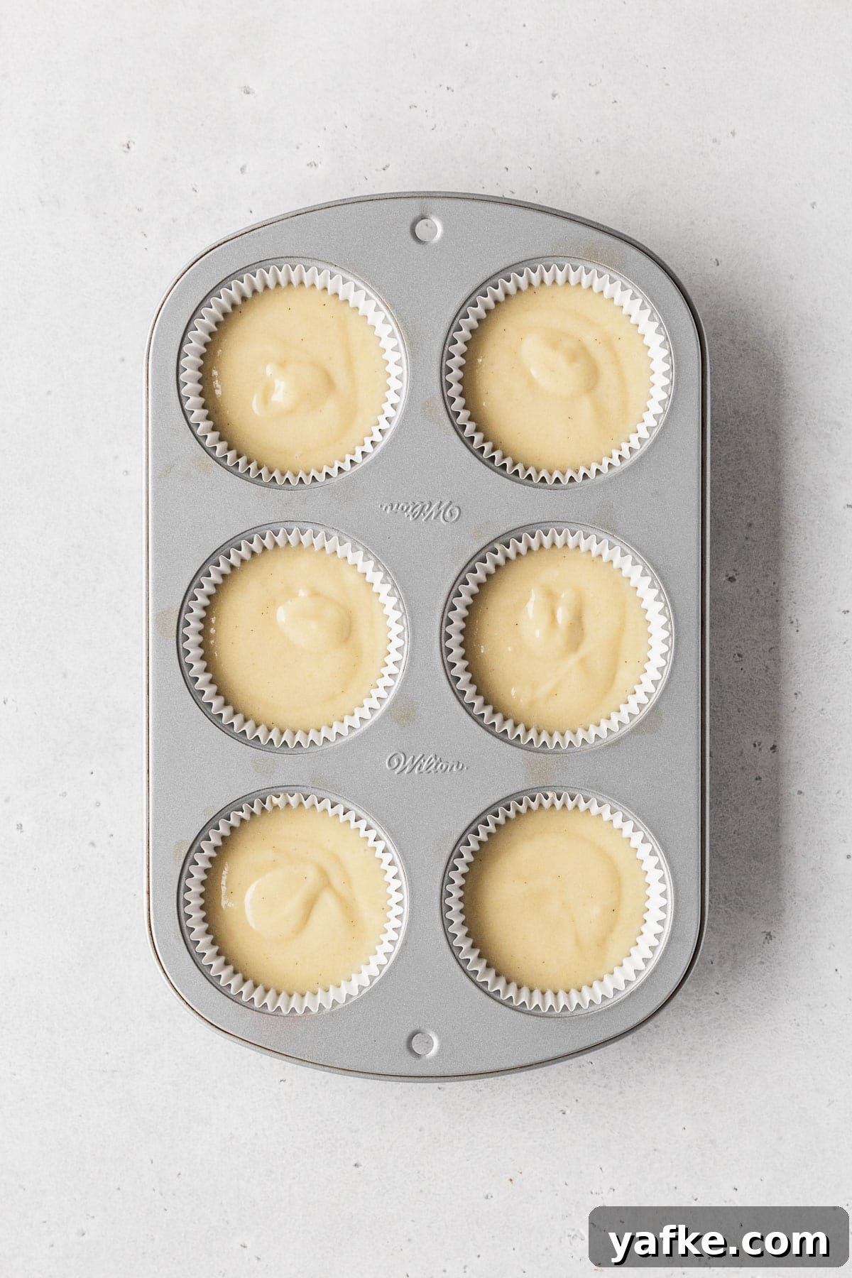 How to Make Dairy-Free Cupcakes 8 Muffin tin filled with white paper liners and dairy-free vanilla cupcake batter before baking.