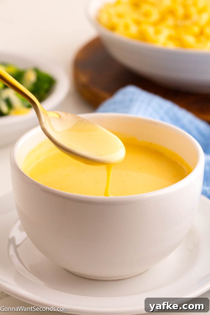 This creamy cheese sauce is a true kitchen staple. Pour it over broccoli, stir it on pasta for quick mac n' cheese, or serve it as a dip for pretzels and chips! #cheesysauce #cheesesauce spoon scooping cheese sauce from a bowl
