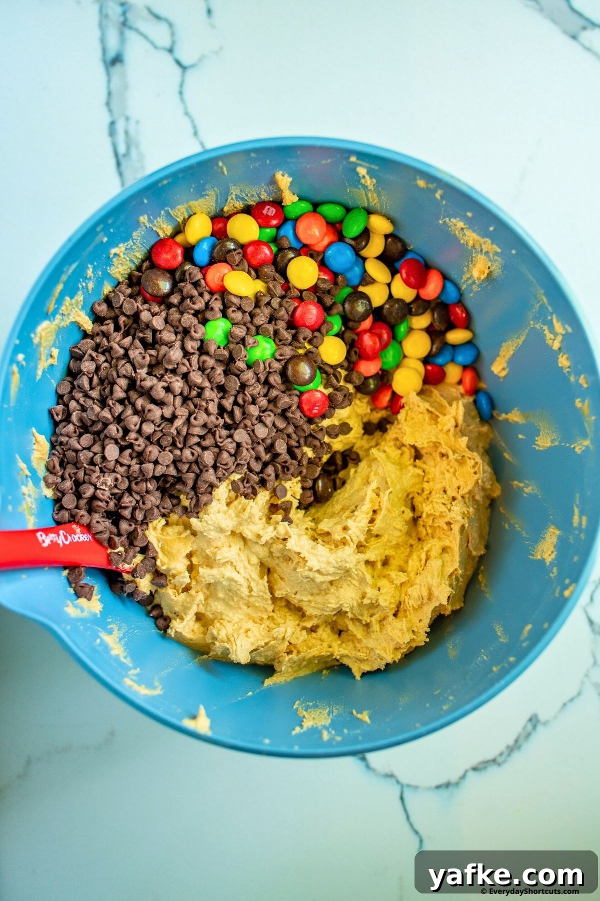 No-Bake Monster Cookie Dough Dip Recipe for Parties 7 chocolate chips and M&M's in a bowl with cookie dough mixture