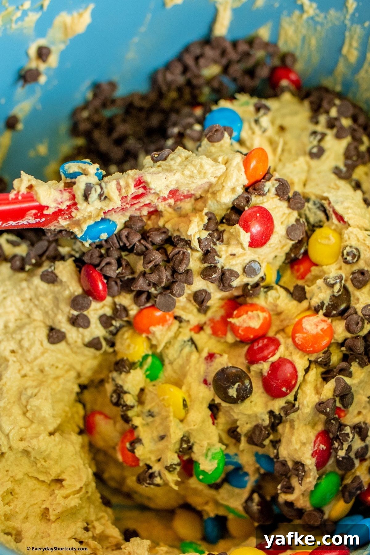 No-Bake Monster Cookie Dough Dip Recipe for Parties 8 folding in chocolate chips and M&M's in a bowl