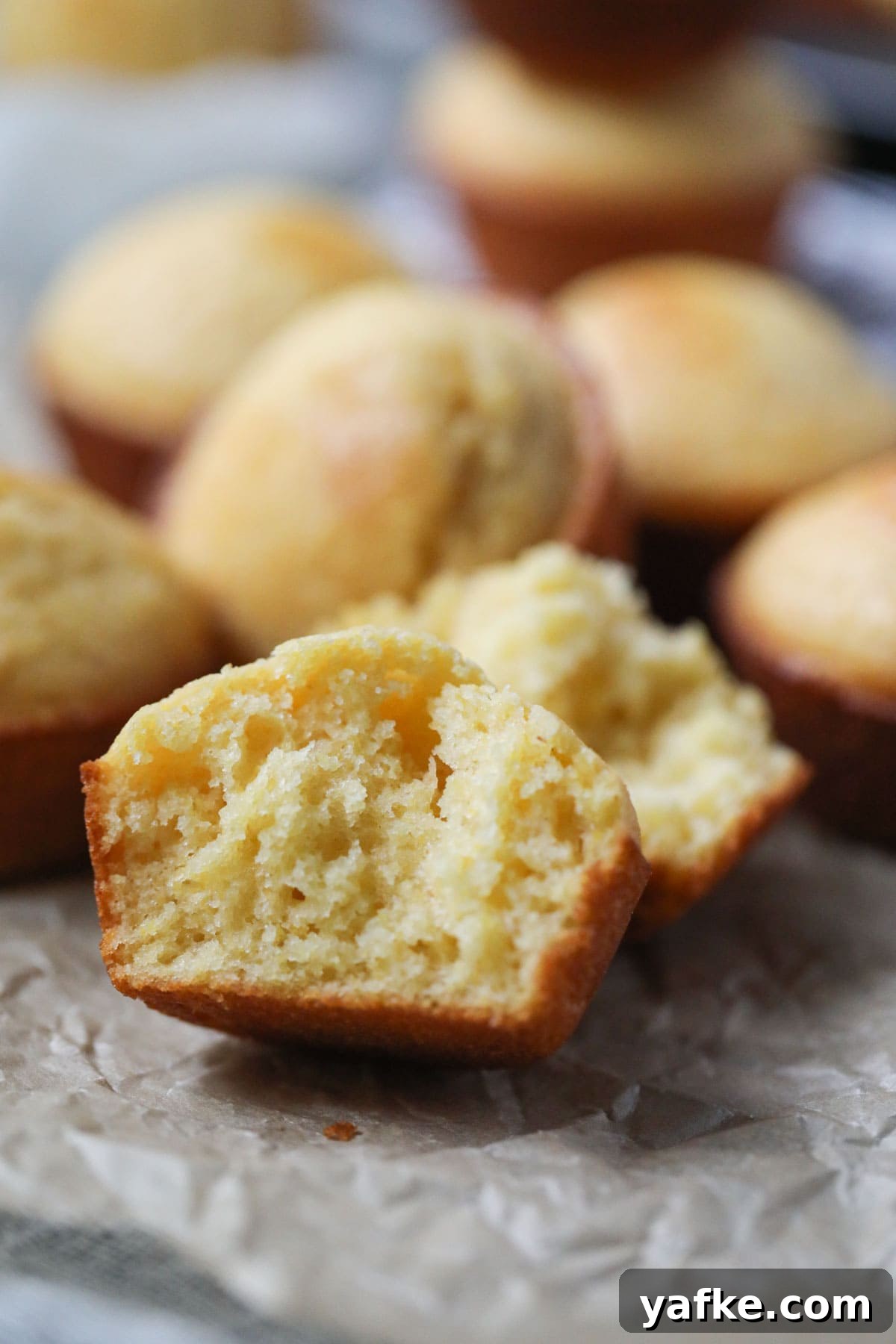 Moist Southern Sweet Cornbread Muffins Recipe 3 buttermilk cornbread muffin sliced open to show texture on parchment paper.