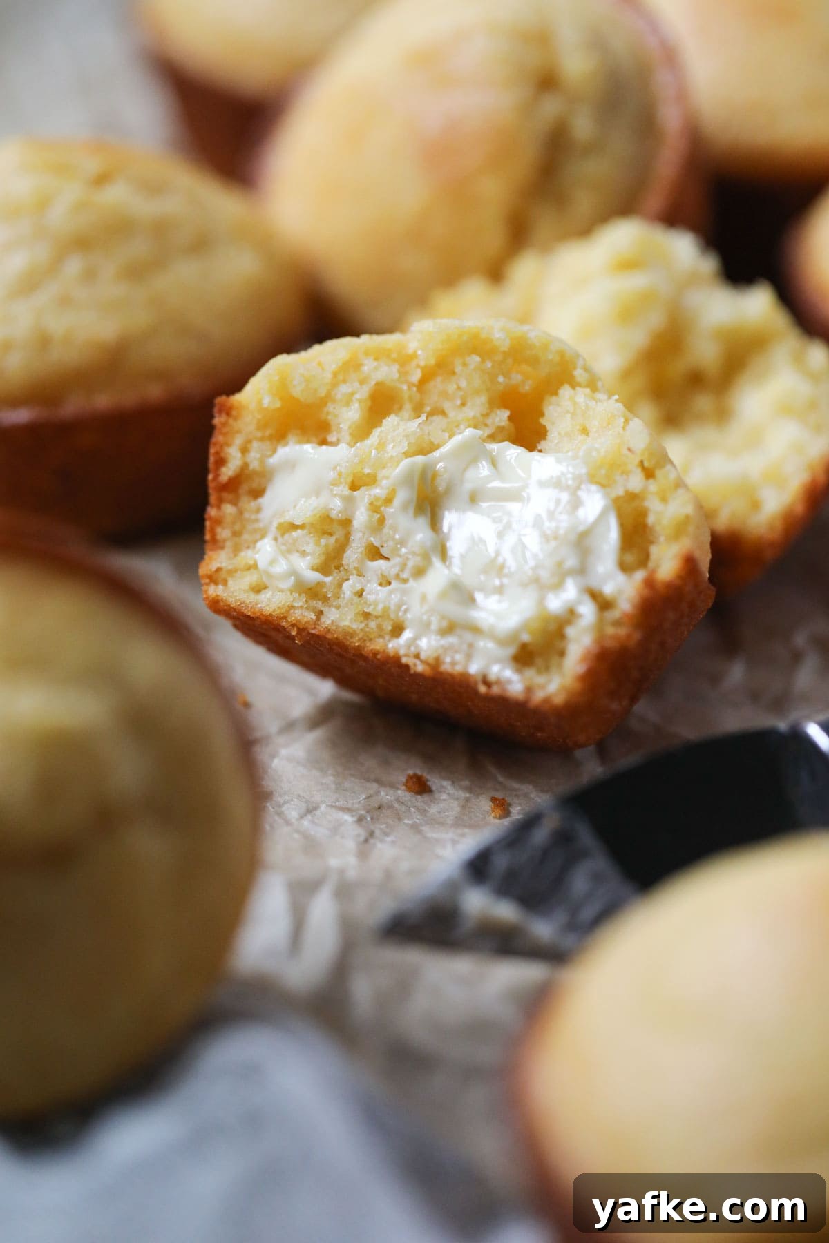 Moist Southern Sweet Cornbread Muffins Recipe 6 buttermilk cornbread muffin sliced open to show texture on parchment paper.