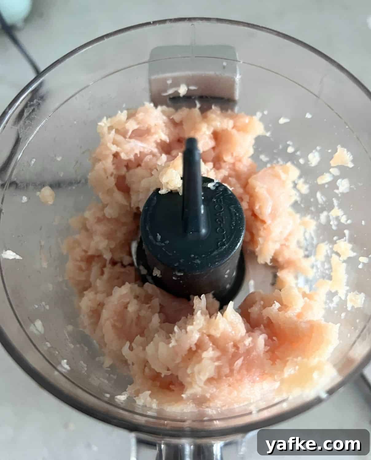 Raw chicken being grinded in a food processor. 