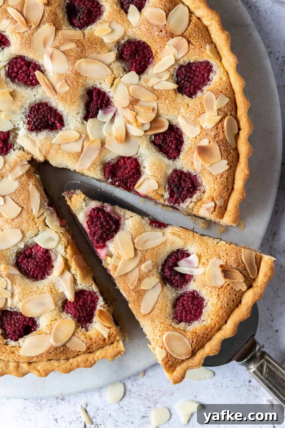 Vegan bakewell tart - a crisp pastry shell filled with raspberry jam, vegan frangipane, fresh raspberries and flaked almonds. Close up of vegan Bakewell tart with a slice cut out.