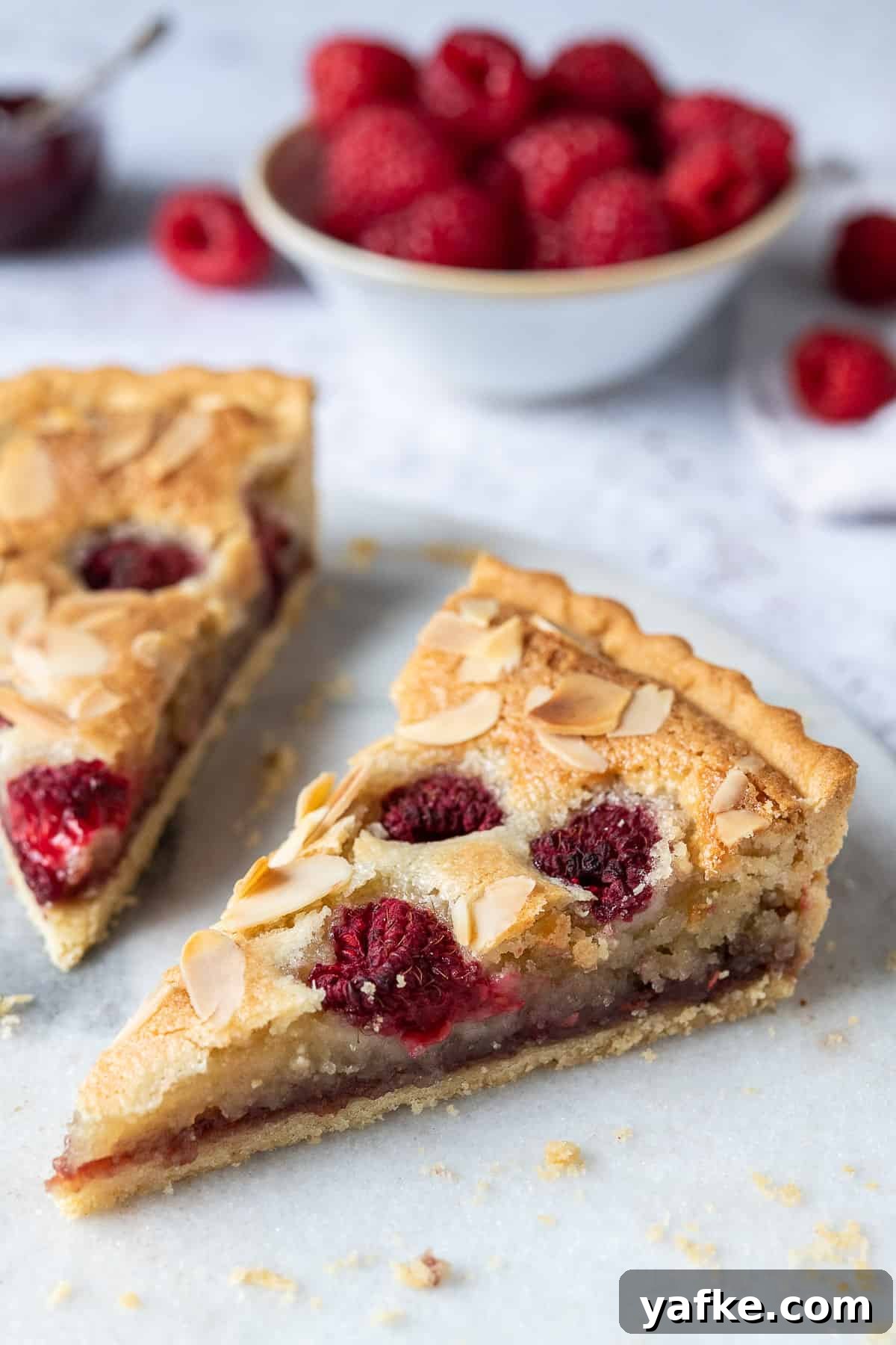 Vegan bakewell tart - a crisp pastry shell filled with raspberry jam, vegan frangipane, fresh raspberries and flaked almonds. Close up of a slice of vegan Bakewell tart