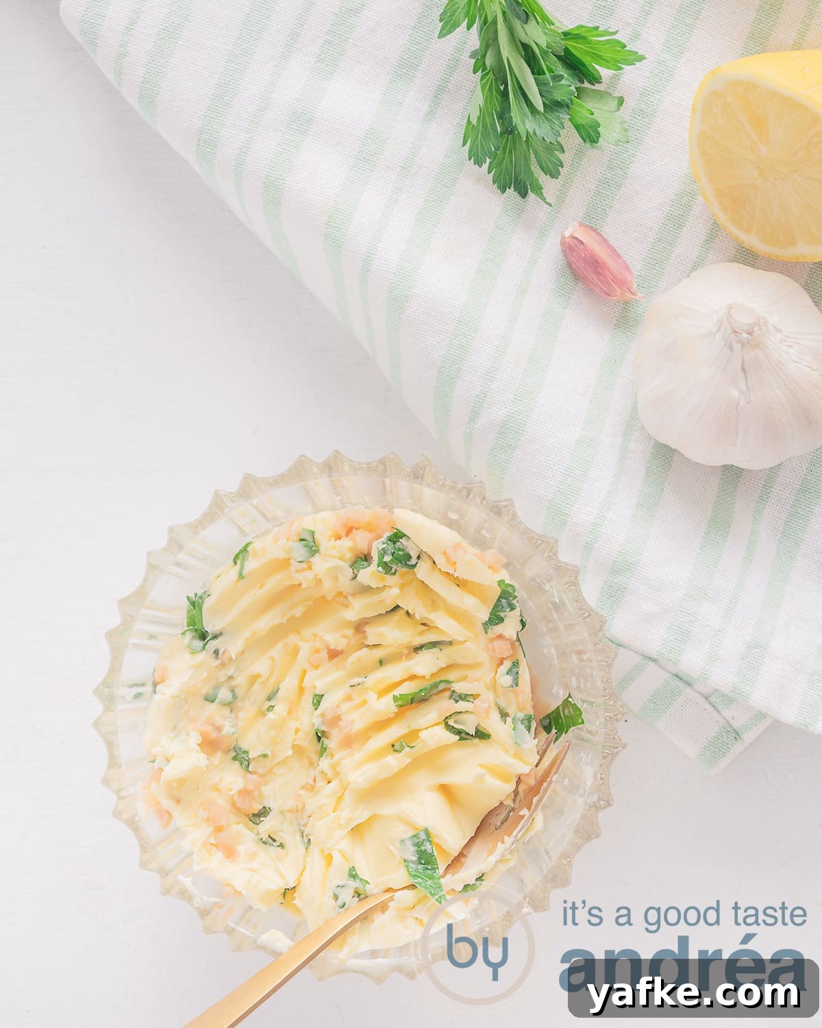 Homemade Garlic Herb Butter Recipe 2 A glass bowl filled with garlic herb butter; garlic, parsley and lemon nearby