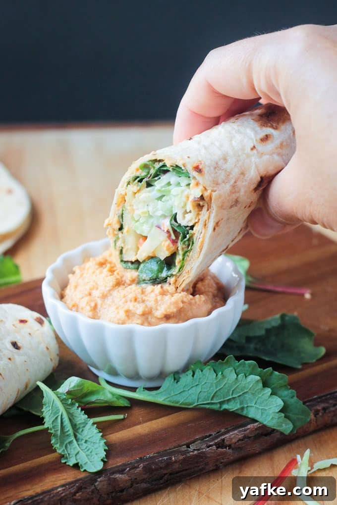 2017's Most Popular Plant-Based Recipes 5 Tortilla veggie wrap dipping into a small white bowl of spicy hummus.