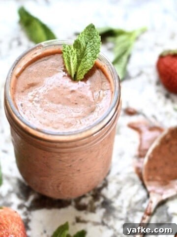 A jar of strawberry basil vinaigrette topped with fresh mint leaves with a spoon beside it.
