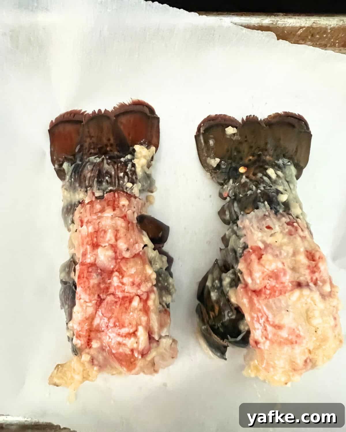 Oven-Baked Lobster Tails with Garlic Butter 5 Lobster tails brushed with butter on a baking sheet.