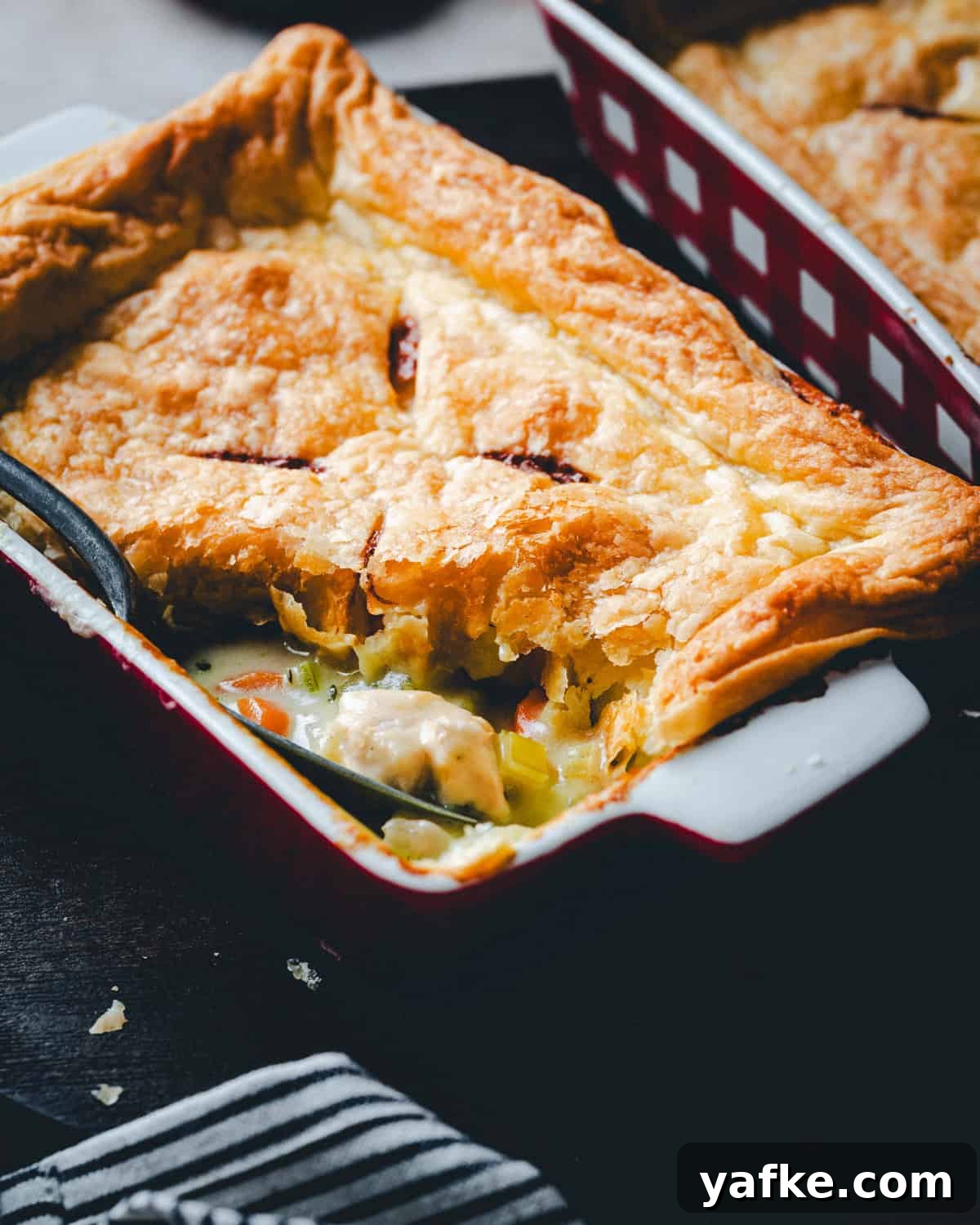 Classic Turkey Pot Pie Recipe with Flaky Golden Crust 2 A close-up of a flaky, golden-brown turkey pot pie with a savory filling of vegetables and turkey, served in a red and white baking dish with a spoon scooping out a portion.