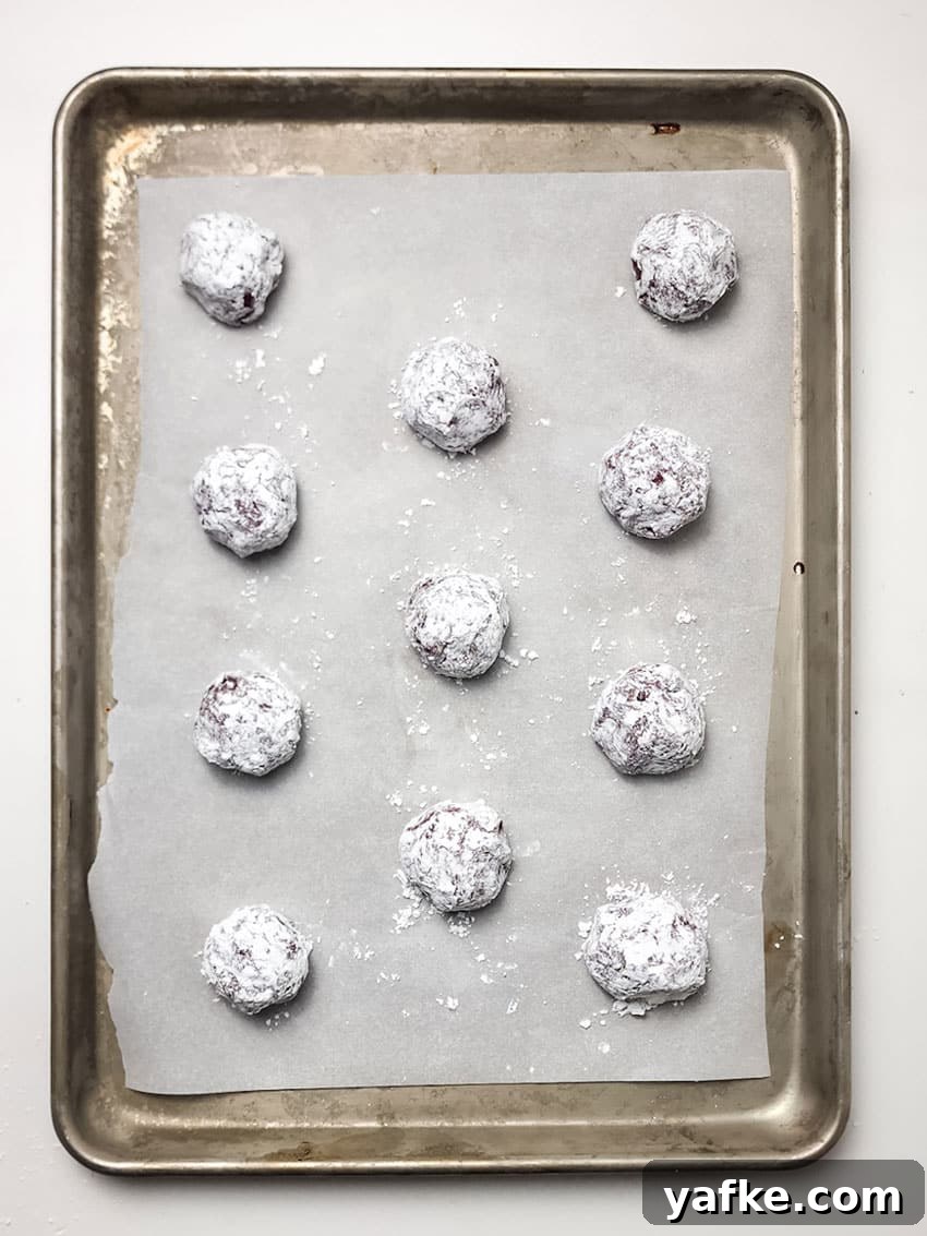 Red Velvet Crinkle Cookies Recipe 4 red velvet crinkle cookies arranged in rows on a parchment paper lined baking sheet