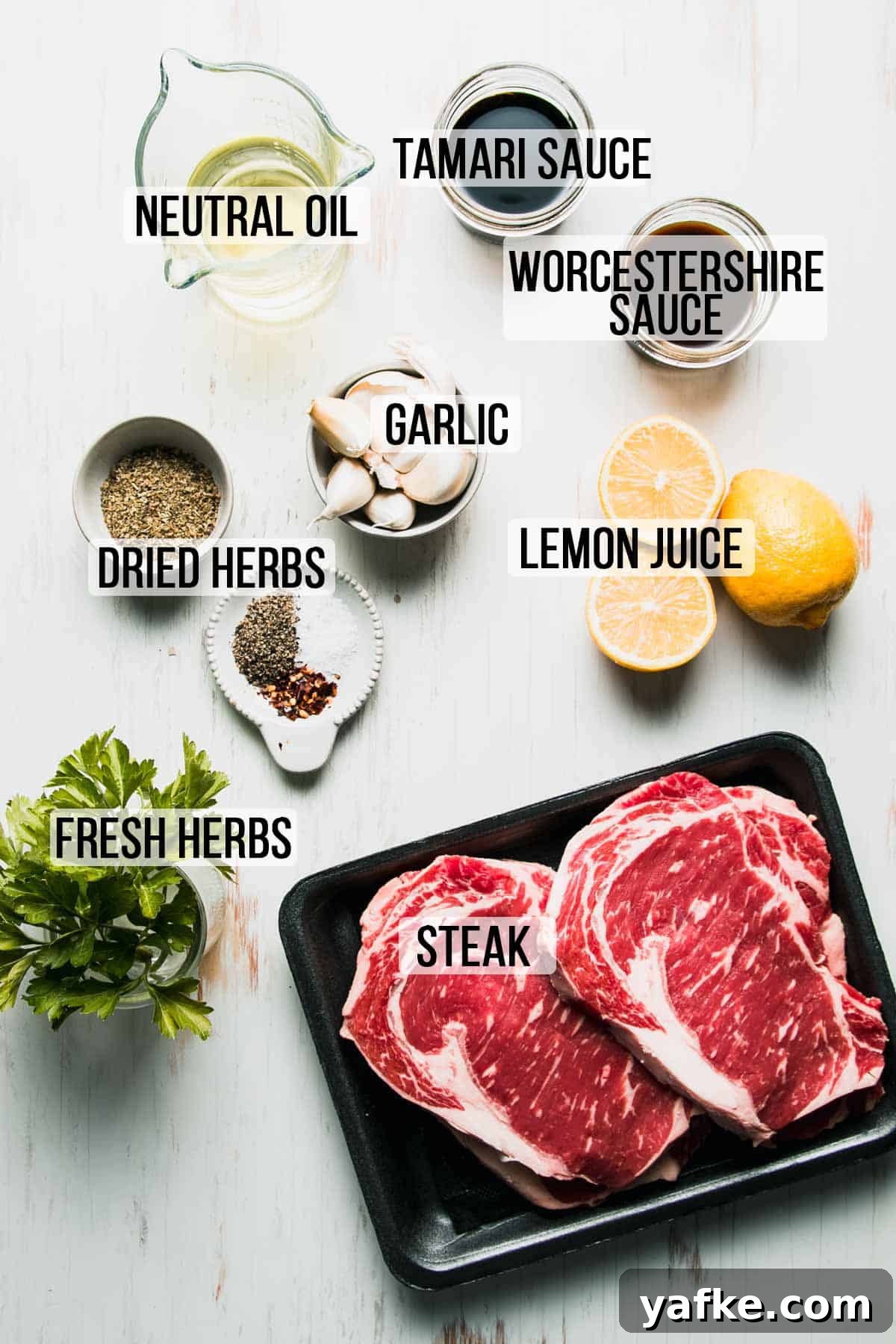 Gluten-Free Steak Marinade Recipe for Juicy Grilled Steak 3 Ingredients for marinade and steak laid out on white wooden surface labeled with text, "neutral oil, Tamari sauce, Worcestershire sauce, garlic, dried herbs, lemon juice, fresh herbs, steak."