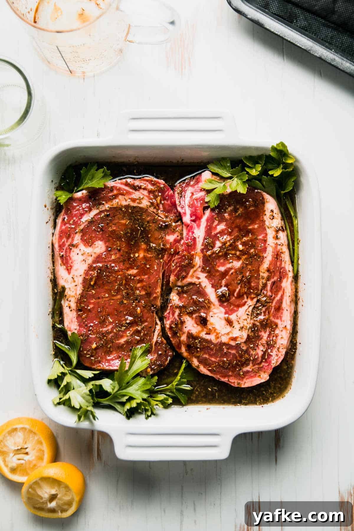 Gluten-Free Steak Marinade Recipe for Juicy Grilled Steak 6 Steaks in square white dish with parsley nudged in corners, squeezed lemon halves next to dish.