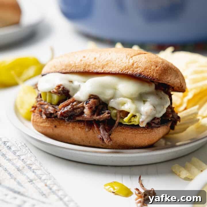 Italian beef sandwich with melted provolone cheese on small plate next to peperoncini peppers.