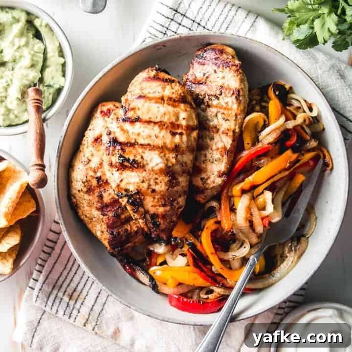 Mexican citrus marinated chicken breasts in a bowl with grilled bell peppers and onions.