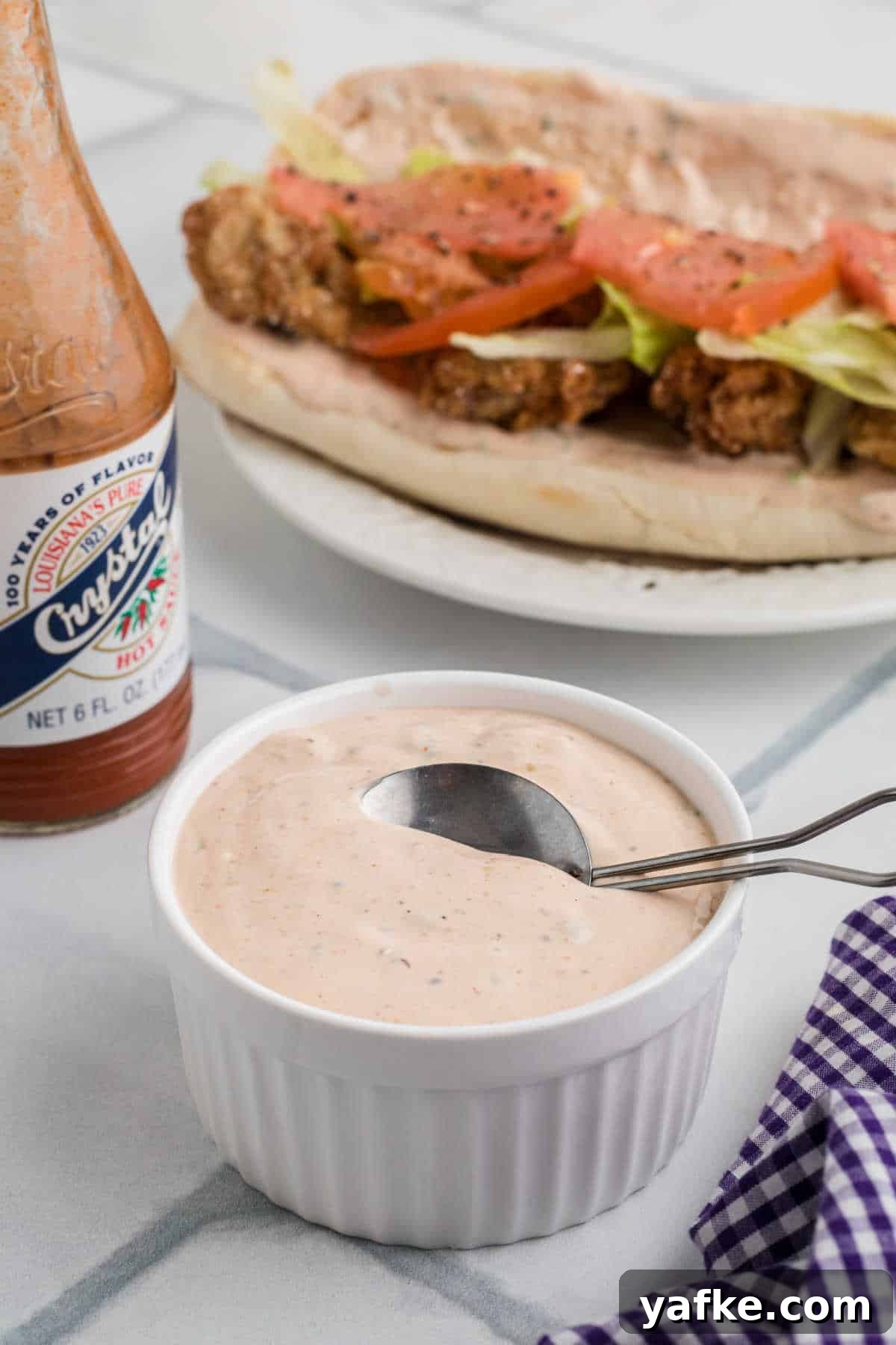 Creamy Remoulade Sauce Recipe for Seafood and Sandwiches 5 Side shot of a bowl of remoulade sauce with an oyster poboy sitting behind.