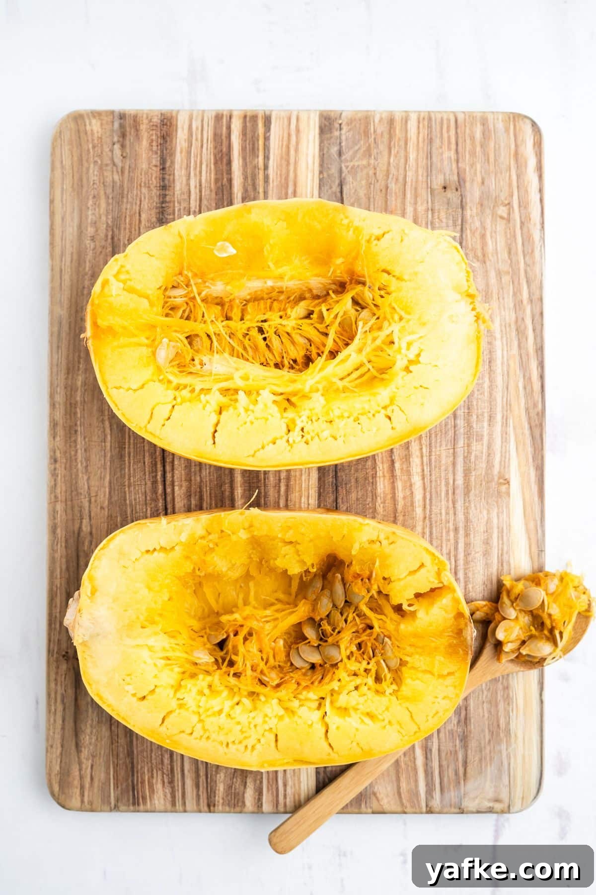 Slow Cooker Spaghetti Squash Recipe 6 Spaghetti squash laid on a wooden cutting board and a spoon removing the seeds.