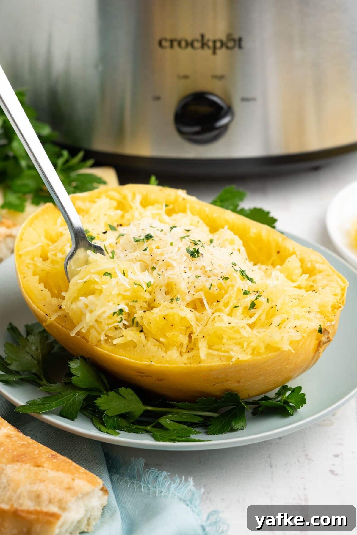Slow Cooker Spaghetti Squash Recipe 10 A fork twirling some of the spaghetti squash up with the plate in front of a crockpot.