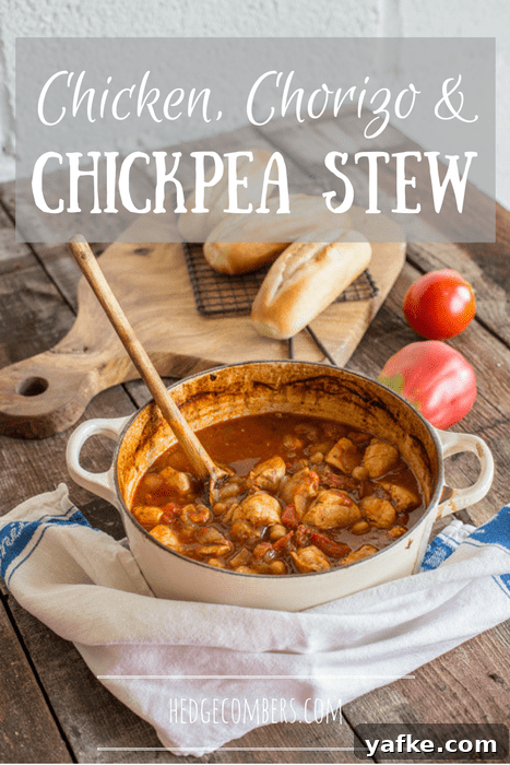 Spanish-Style Chicken, Chorizo, and Chickpea Stew 2 wooden surface with white plan of chicken stew, small baked baguettes and large tomatoes