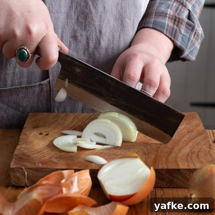 Spanish-Style Chicken, Chorizo, and Chickpea Stew 4 womans hands slicing a white onion on a wooden kitchen board