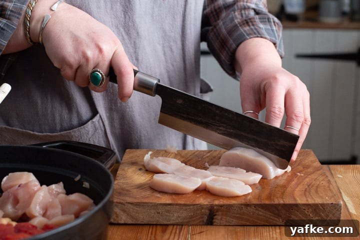 Spanish-Style Chicken, Chorizo, and Chickpea Stew 6 womans hands chopping chicken breasts on a wooden board