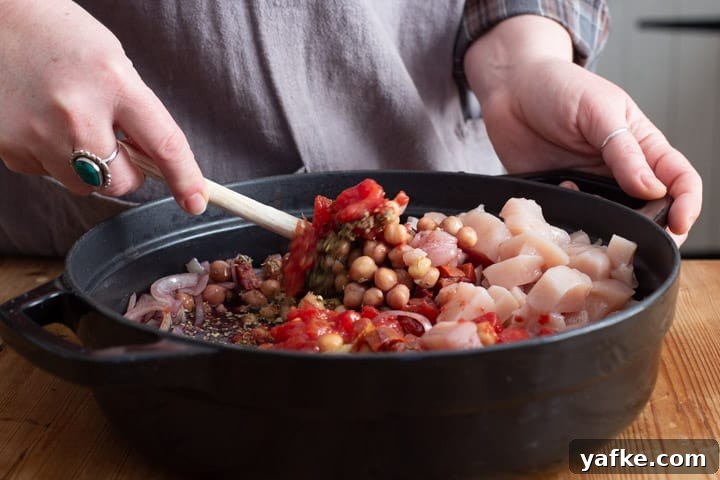 Spanish-Style Chicken, Chorizo, and Chickpea Stew 10 womans hands stirring the raw ingredients in a black pan of chicken chorizo and chickpea stew