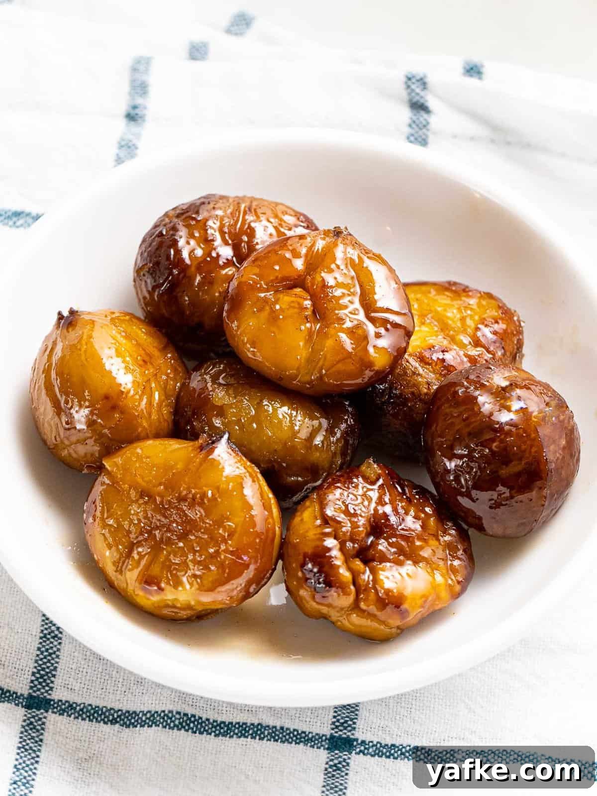 How to Make Quick Candied Chestnuts (Marrons Glacés) 2 Quick candied chestnuts in spiced cinnamon sugar glaze in a white bowl.