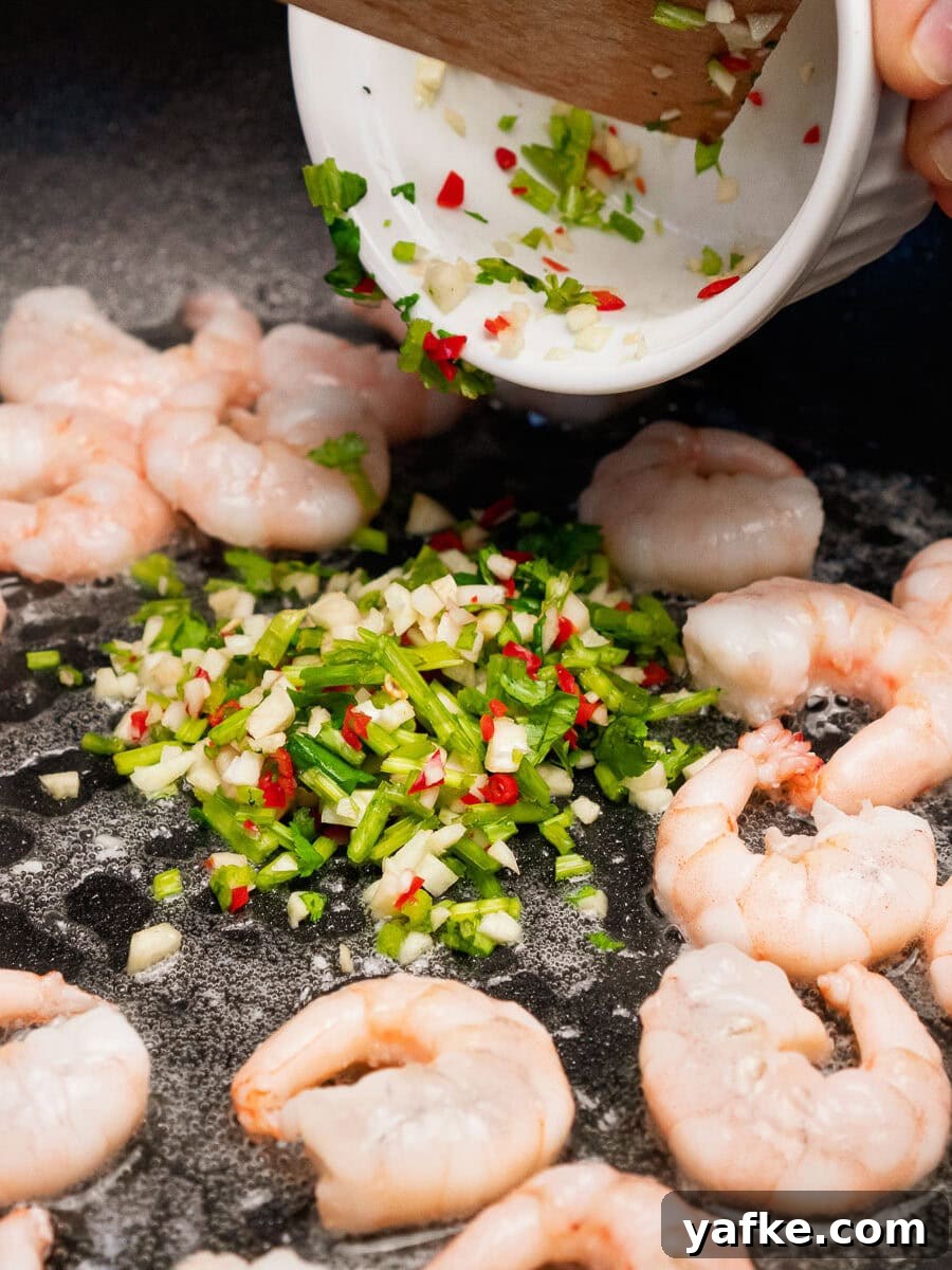 Crispy Shrimp Tacos with Sweet Chili Sauce 12 King prawns frying in oil in a pan with chopped chillies, garlic and coriander being poured on top