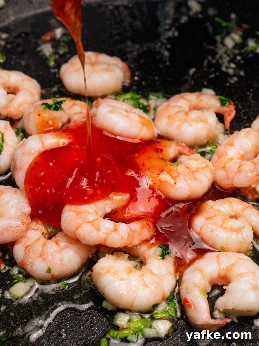 Crispy Shrimp Tacos with Sweet Chili Sauce 13 Sweet chilli sauce being poured over the top of king prawns frying in a pan