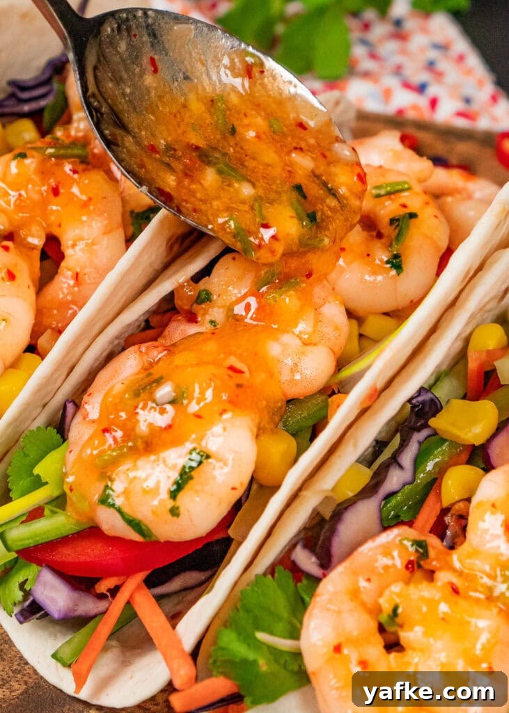 Crispy Shrimp Tacos with Sweet Chili Sauce 15 sweet chilli sauce being spooned over the top of king prawns in filled taco wraps filled with salad