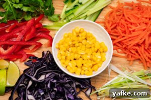Crispy Shrimp Tacos with Sweet Chili Sauce 3 Grated red cabbage, sliced spring onion, grated carrot, sliced cucumber fresh coriander , sliced red pepper wedges of lime and sweet corn in a white bowl all served on a wooden chopping board