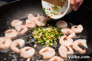 Crispy Shrimp Tacos with Sweet Chili Sauce 6 King prawns frying in oil in a pan with chopped chillies, garlic and coriander being poured on top