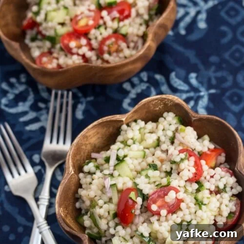 Overhead view of Israeli couscous tabbouleh in 2 bowls with forks alongside.