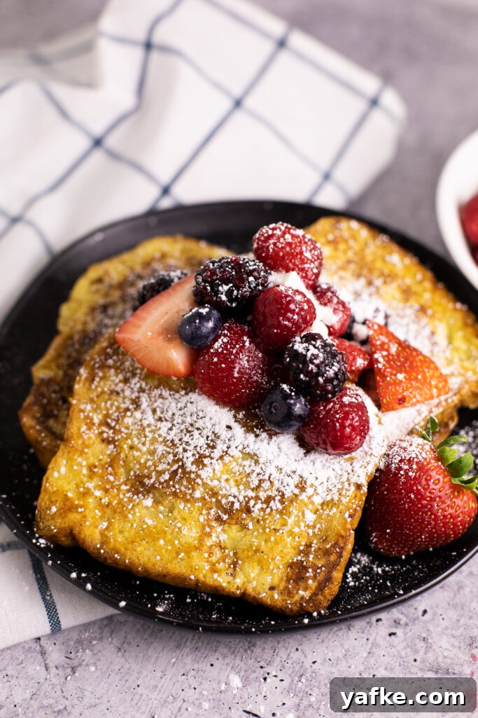 Cinnamon French Toast Recipe with Maple Syrup Glaze 2 Three pieces of cinnamon French toast on a black plate topped with strawberries, blueberries, blackberries, raspberries, and powdered sugar.