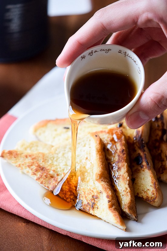 Cinnamon French Toast Recipe with Maple Syrup Glaze 3 2 pieces of Cinnamon French toast cut into triangles with maple syrup being poured over top.
