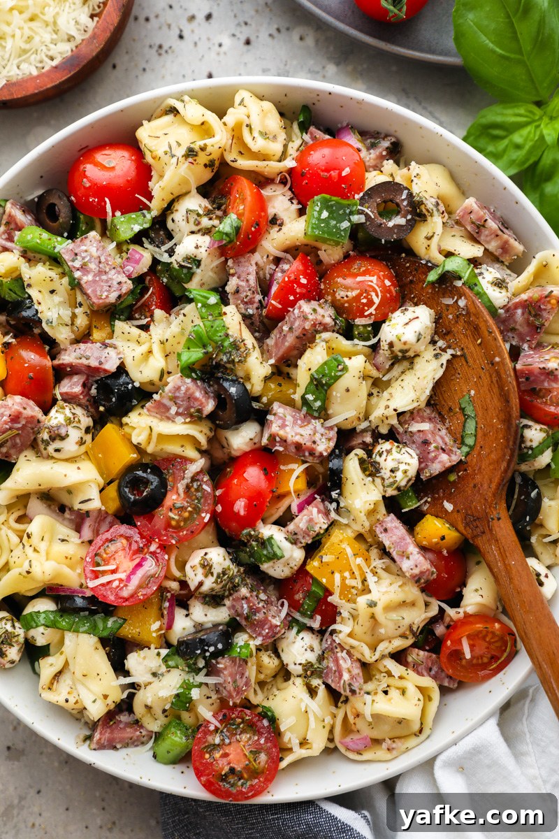 Italian Tortellini Pasta Salad Recipe 6 A bowl filled with Italian tortellini pasta salad surrounded by a small bowl of shredded parmesan, fresh basil and cherry tomatoes
