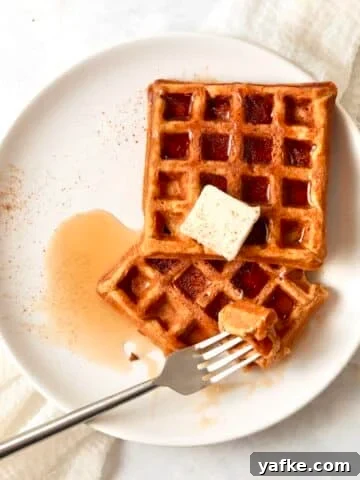 Single serve pumpkin waffles on a plate with maple syrup and butter.