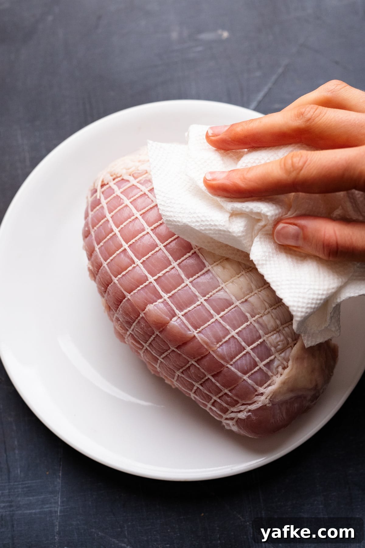 Juicy Maple Herb Air Fryer Turkey Breast 4 Hands patting paper towels on a turkey breast that's sitting on a white plate on a gray background.