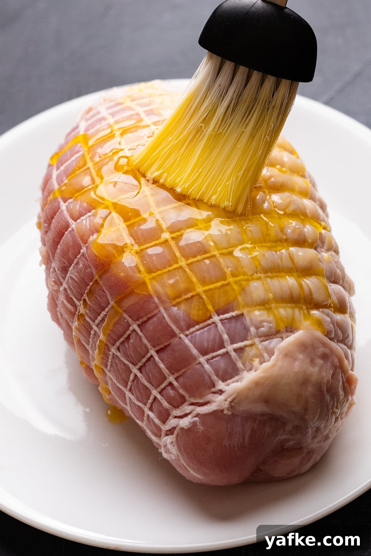 Juicy Maple Herb Air Fryer Turkey Breast 5 A brush basting melted butter on a turkey breast that's sitting on a white plate.