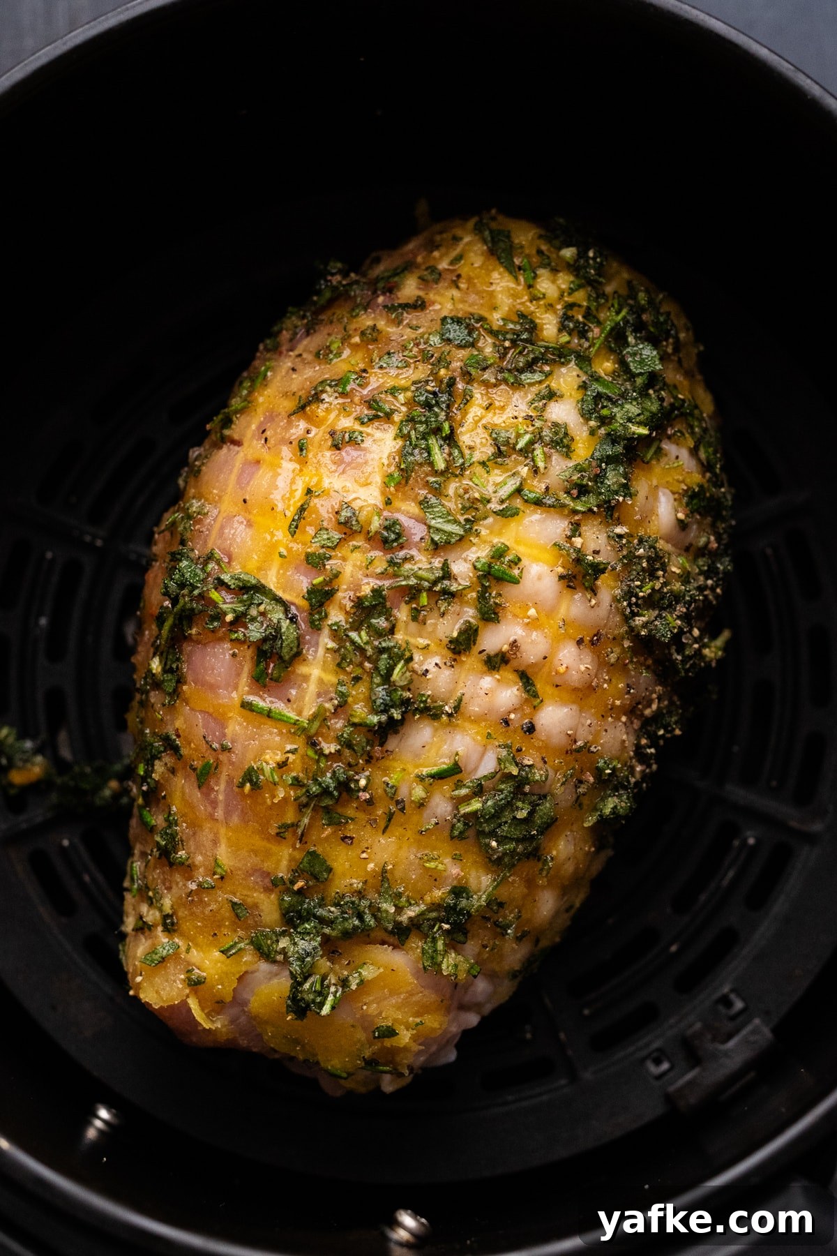 Juicy Maple Herb Air Fryer Turkey Breast 6 A turkey breast with chopped herbs on it in a black air fryer basket.