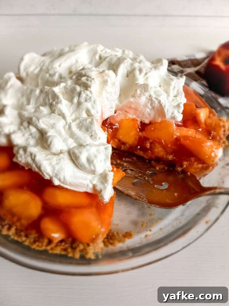 How to Make Authentic Amish Fresh Peach Pie 7 a whole Amish peach pie with graham cracker crust and whipped cream, with a slice removed.