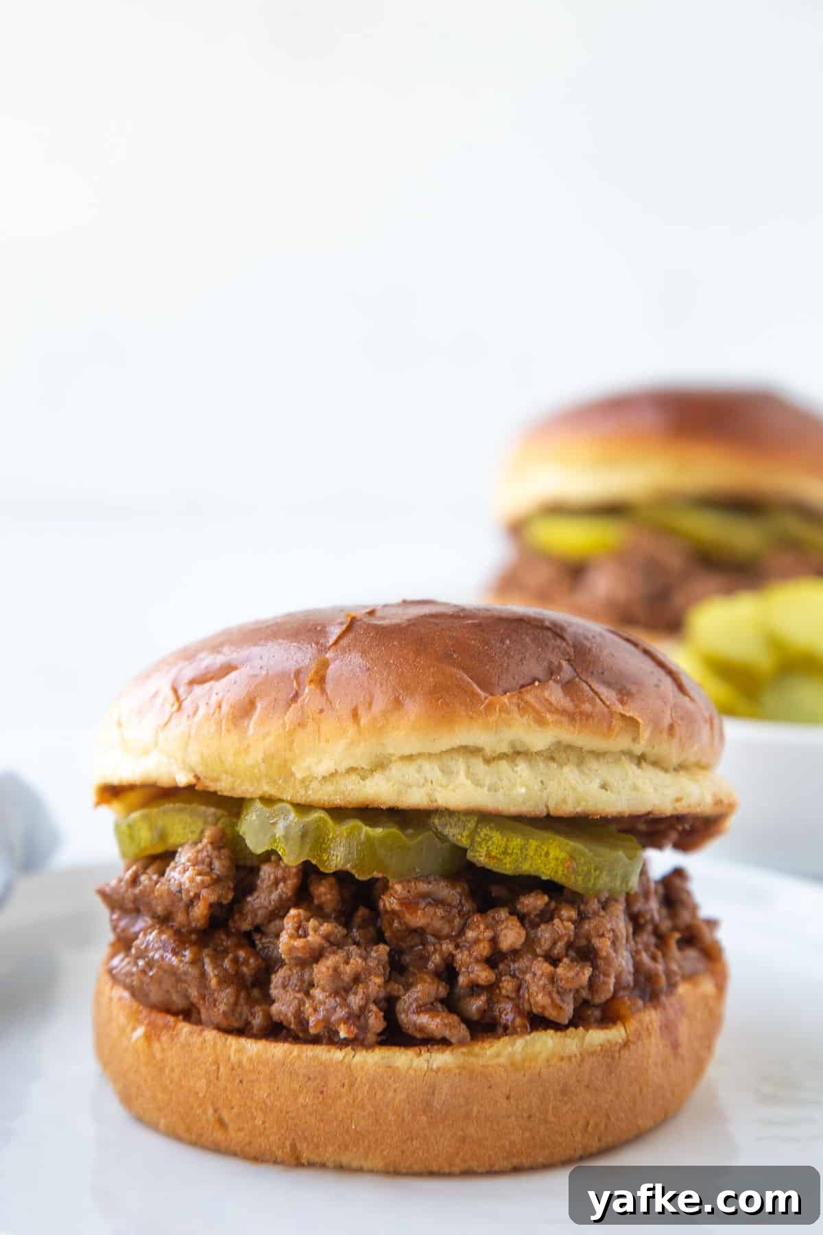 Classic Old Fashioned Sloppy Joes Sandwich Recipe 2 old fashioned sloppy joe sandwich on brioche with pickle chips, sitting on a white plate.