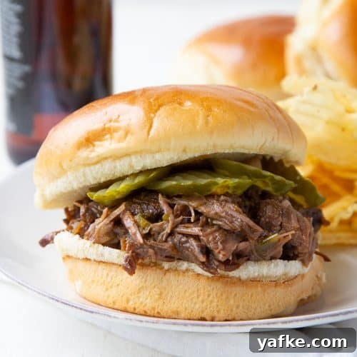 Classic Old Fashioned Sloppy Joes Sandwich Recipe 9 shredded beef with pickles on a brioche bun on a white plate.
