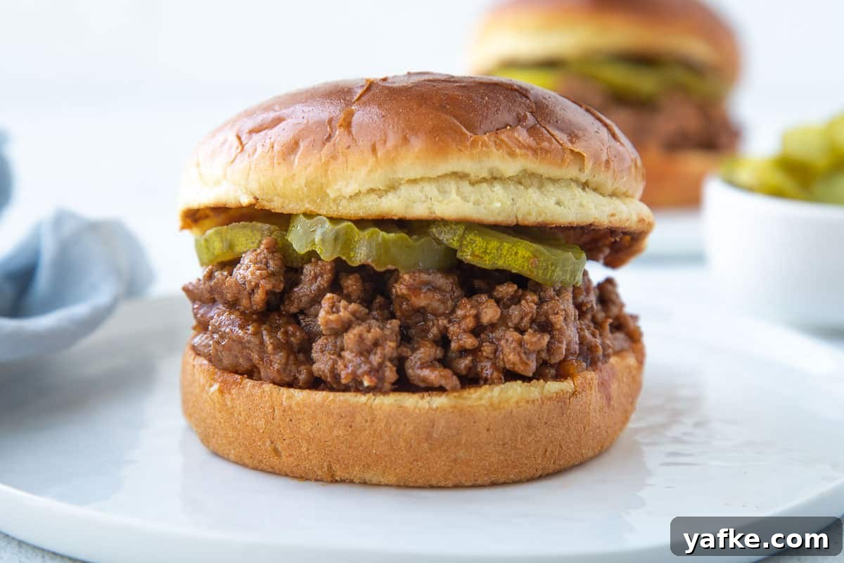 Classic Old Fashioned Sloppy Joes Sandwich Recipe 7 old fashioned sloppy joe sandwich on a brioche bun with pickles on a white plate.