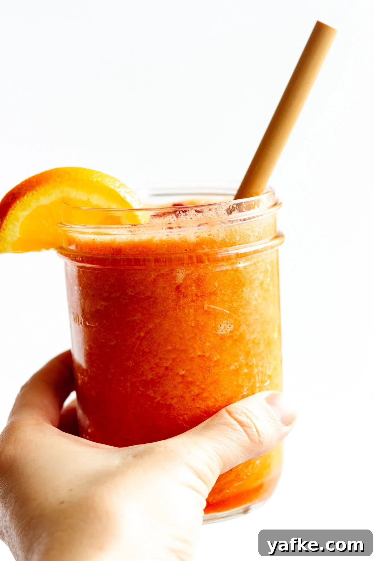Vitamin C Boost Smoothie with Citrus and Berries 2 Hand holding mason jar filled with Vitamin C Smoothie with an orange slice on the edge and bamboo straw.