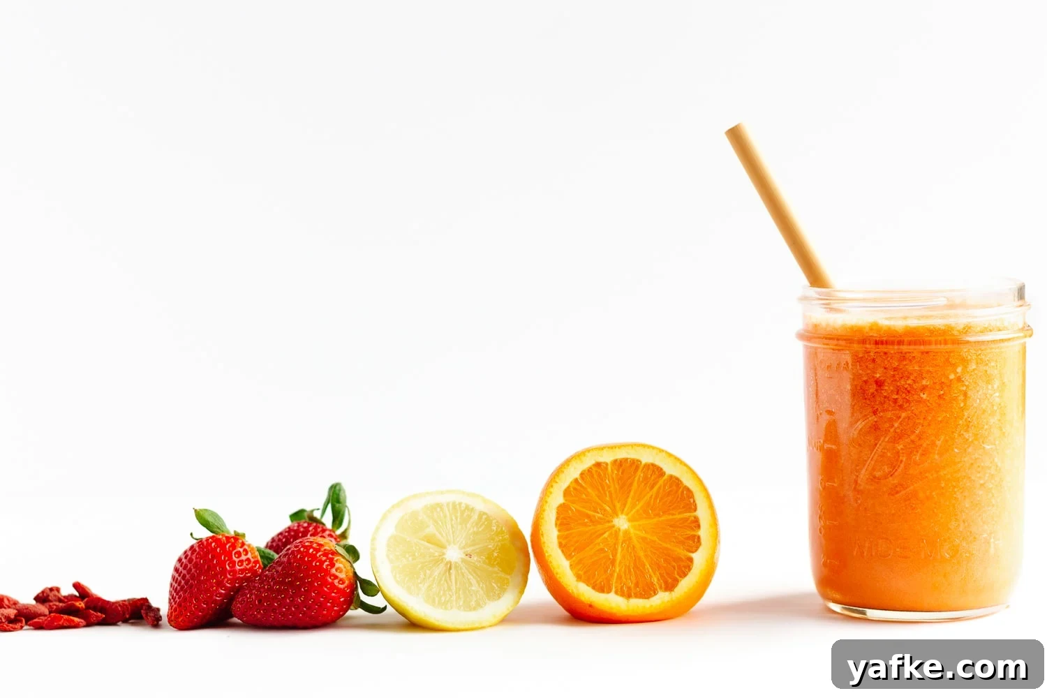 Vitamin C Boost Smoothie with Citrus and Berries 3 Goji berries, strawberries, lemon, orange and glass of Vitamin C Smoothie lined up on a white background.