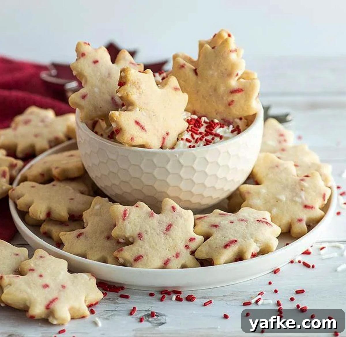 21 Patriotic Canada Day Desserts 11 maple shaped cookies with cream cheese dip in a white bowl, with red sprinkles all around